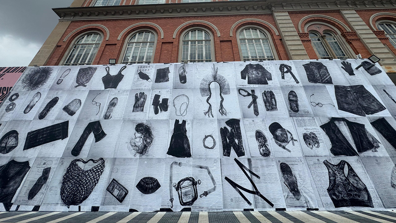 A mural depicting various items of clothing in black and white hangs on a large brick building.
