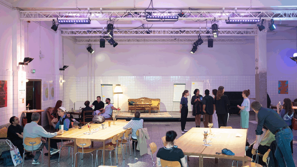 Sixteen people are standing or sitting in small groups, talking in a large room.