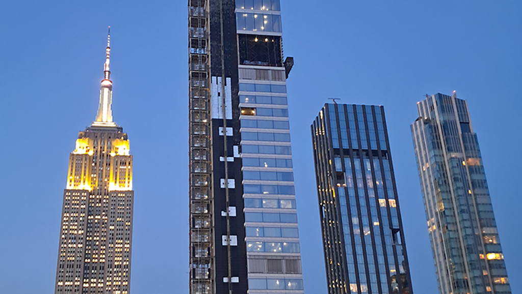 Three skyscrapers in front of a blue night sky, the empire state building on the left.