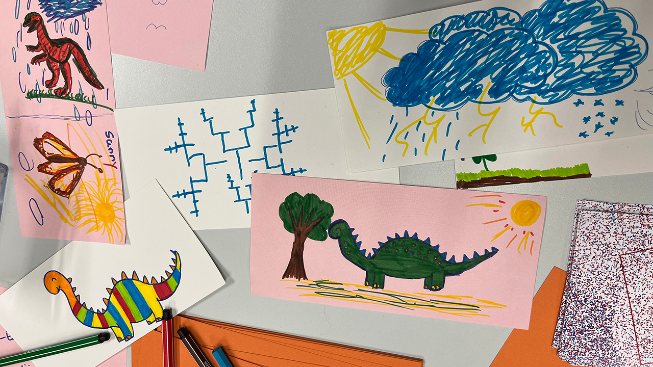 Fourteen rectangular pieces of paper with hand-drawn motifs, such as butterflies, clouds, suns, and dinosaurs, lie on a white surface.